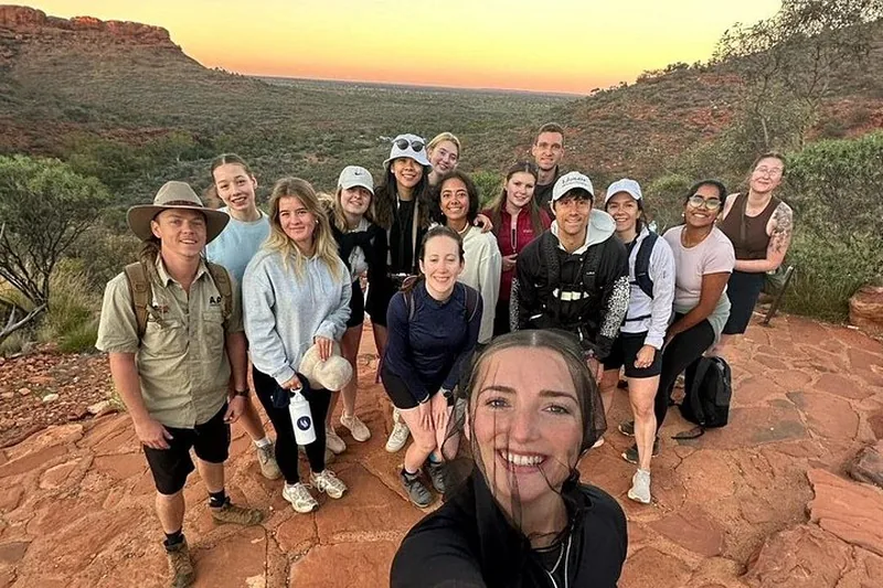 Camping safari group smiling on red rock at sunset on a multi-day Uluru tour with Kings Canyon, Northern Territory Australia